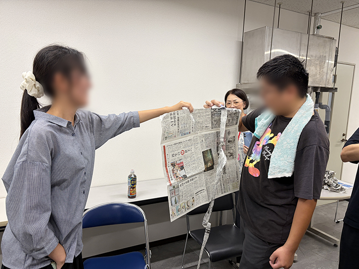 コミュニケーションを図りながら新聞紙が途中で切れないよう慎重に片手で破り進める、2人1組のペアワークの様子。