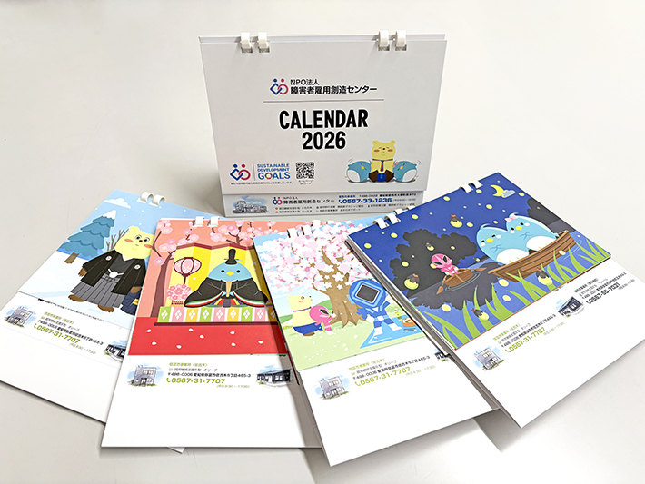 事業所オリジナルの2026年卓上カレンダーと、マスコットキャラクター（障害者雇用創造レンジャーなど）が描かれた季節のイラストカード。地域の方々や関係機関から毎年好評を得ているかわいいデザインの卓上カレンダー。