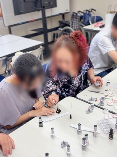 作業中、作業に慣れている訓練生が隣の席の参加者に向けて優しくアドバイスやコツを伝えている相互支援の様子。